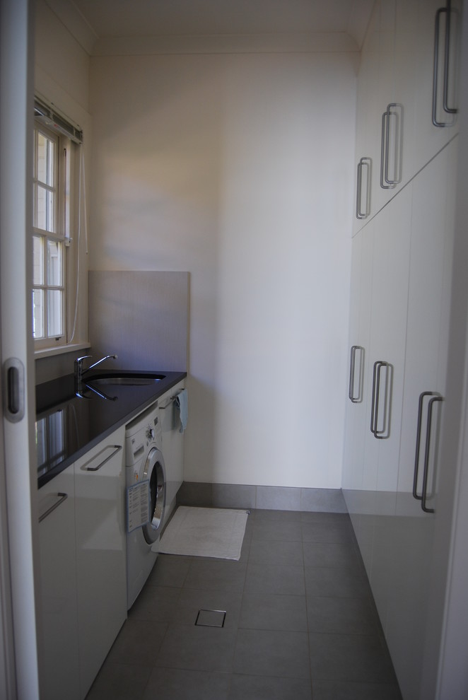 This is an example of a large contemporary galley dedicated laundry room in Sydney with an undermount sink, flat-panel cabinets, white cabinets, granite benchtops, white walls, ceramic floors and a side-by-side washer and dryer.