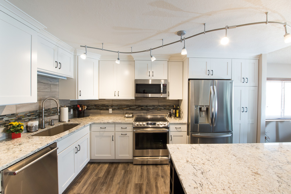 Inspiration for a small transitional l-shaped brown floor and laminate floor open concept kitchen remodel with an undermount sink, shaker cabinets, white cabinets, granite countertops, beige backsplash, matchstick tile backsplash, stainless steel appliances and an island
