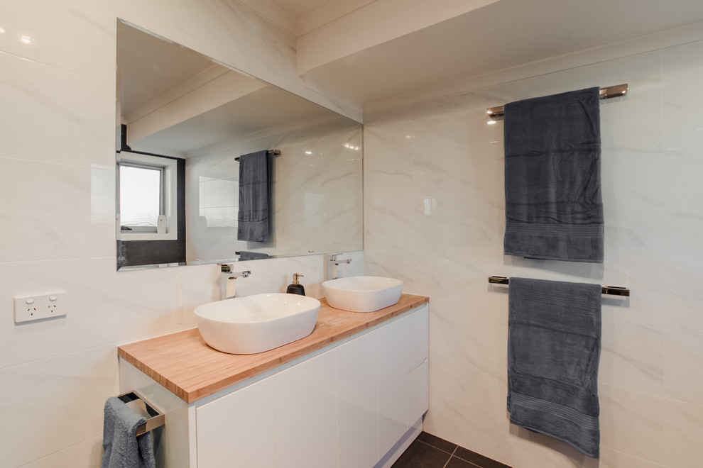 Inspiration for a mid-sized contemporary master bathroom in Adelaide with flat-panel cabinets, white cabinets, a corner shower, a two-piece toilet, white tile, ceramic tile, white walls, ceramic floors, a vessel sink, wood benchtops, grey floor and a hinged shower door.