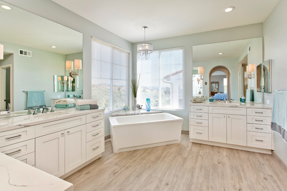 Photo of a large beach style master bathroom in Tampa with shaker cabinets, white cabinets, a freestanding tub, a two-piece toilet, porcelain tile, blue walls, porcelain floors, an undermount sink, engineered quartz benchtops and beige floor.