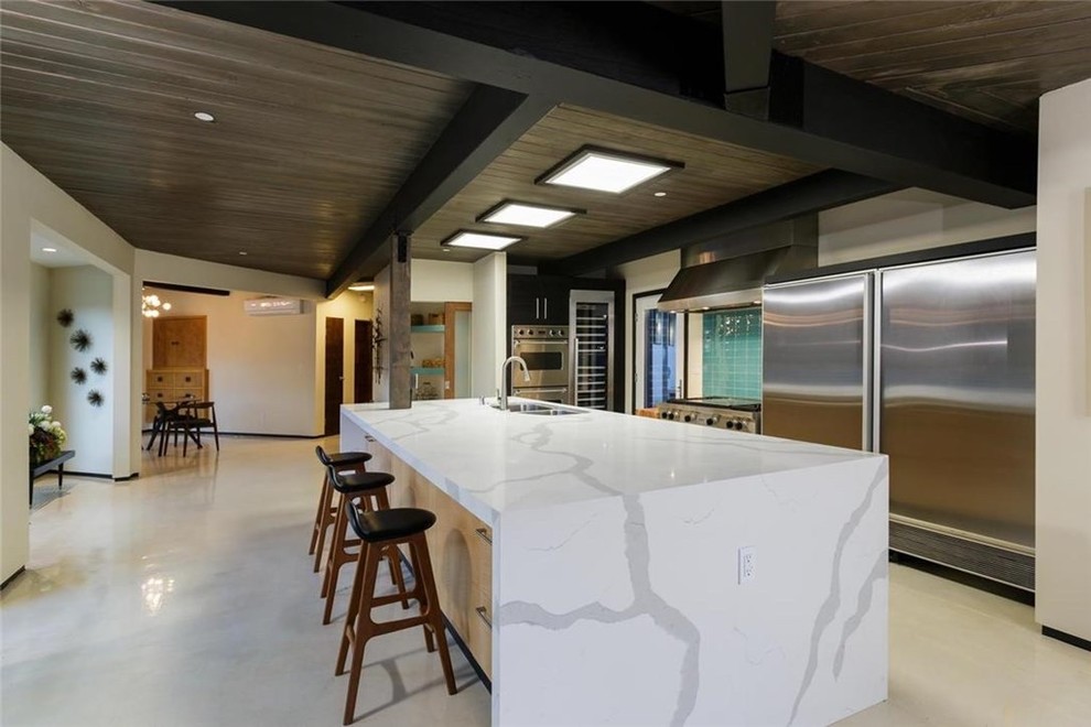 Large modern galley kitchen in Los Angeles with a drop-in sink, flat-panel cabinets, black cabinets, marble benchtops, ceramic splashback, stainless steel appliances, limestone floors and with island.