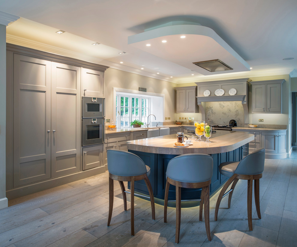 Inspiration for a large country l-shaped kitchen in Dublin with a farmhouse sink, recessed-panel cabinets, marble benchtops, grey splashback, stone tile splashback, stainless steel appliances, light hardwood floors, with island and grey cabinets.