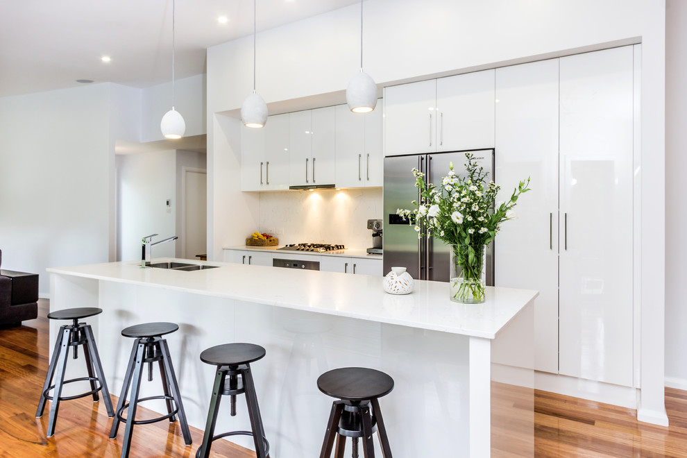 This is an example of a contemporary galley open plan kitchen in Wollongong with stone slab splashback, flat-panel cabinets, white cabinets and with island.