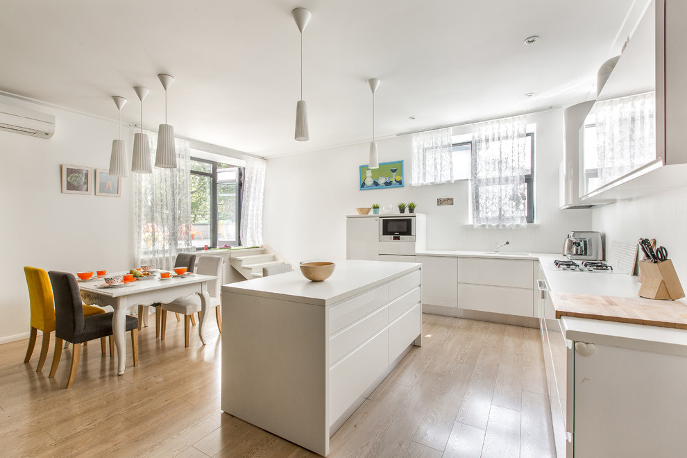 Design ideas for a contemporary l-shaped eat-in kitchen in Other with flat-panel cabinets, white cabinets, solid surface benchtops, white splashback, white appliances, with island and light hardwood floors.