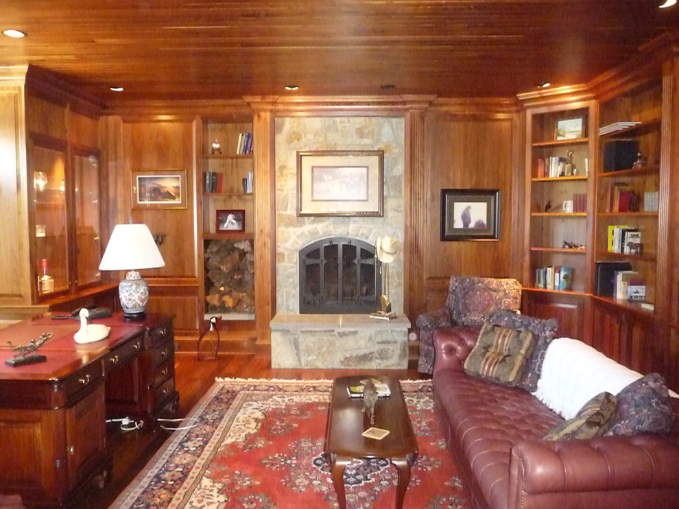 Mid-sized traditional home office in DC Metro with a library, brown walls, medium hardwood floors, a standard fireplace, a stone fireplace surround, a freestanding desk and brown floor.