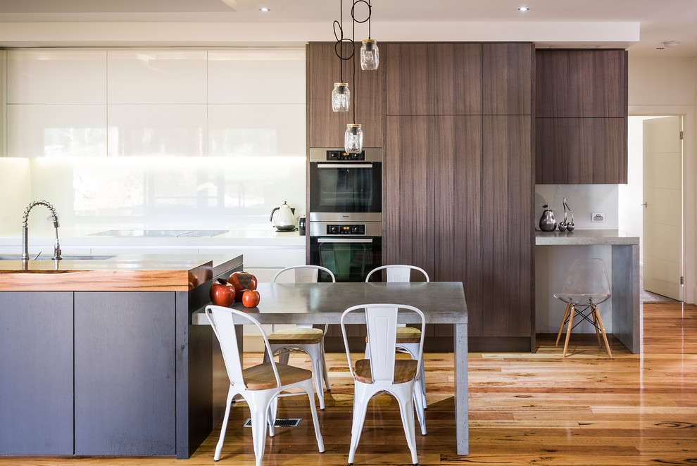 Design ideas for a contemporary galley kitchen in Melbourne with flat-panel cabinets, dark wood cabinets, panelled appliances, medium hardwood floors and with island.