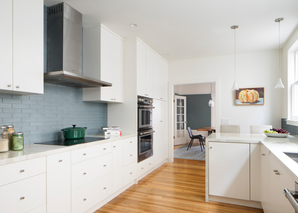 Bild på ett mellanstort funkis vit vitt kök, med en undermonterad diskho, släta luckor, vita skåp, marmorbänkskiva, grått stänkskydd, stänkskydd i tunnelbanekakel, rostfria vitvaror, mellanmörkt trägolv, en halv köksö och flerfärgat golv