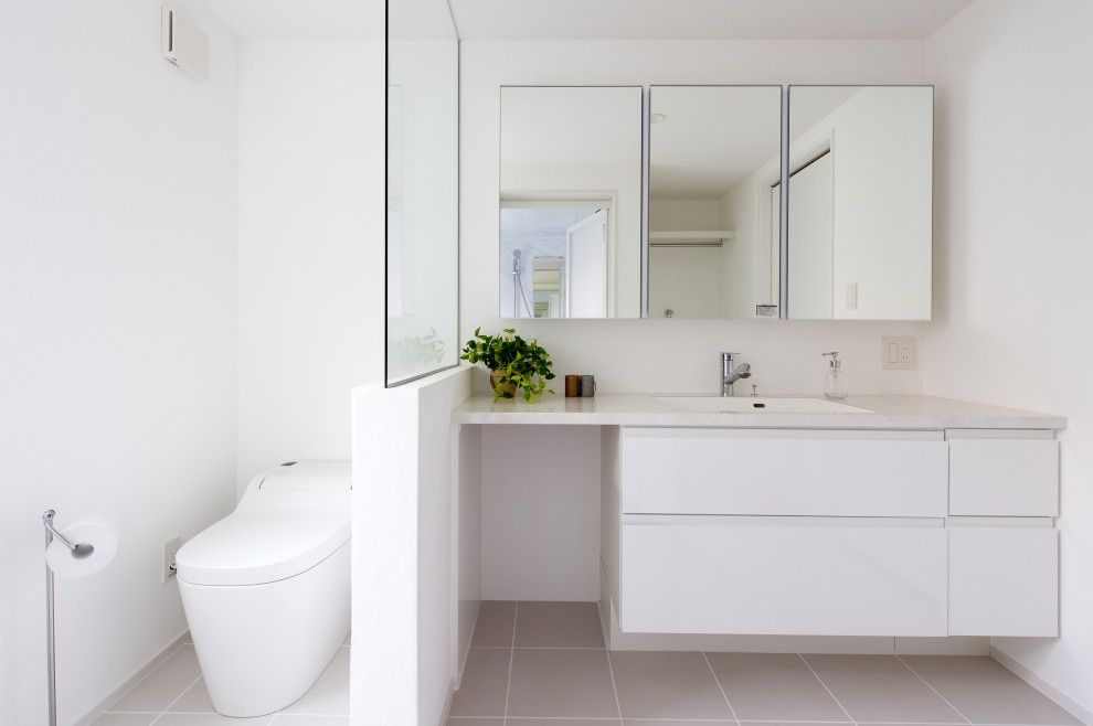 This is an example of a mid-sized asian bathroom in Other with beaded inset cabinets, white cabinets, a one-piece toilet, white walls, an integrated sink, solid surface benchtops, beige floor, grey benchtops, a built-in vanity and wallpaper.