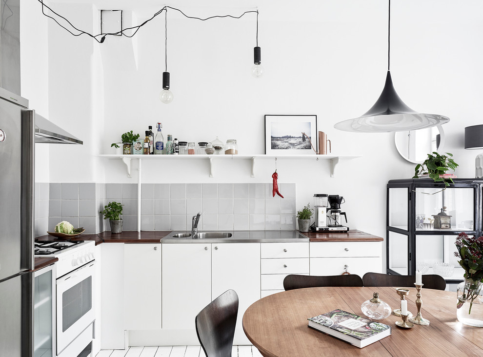 Mid-sized scandinavian l-shaped eat-in kitchen in Gothenburg with a double-bowl sink, flat-panel cabinets, white cabinets, wood benchtops, grey splashback, painted wood floors, no island and stainless steel appliances.