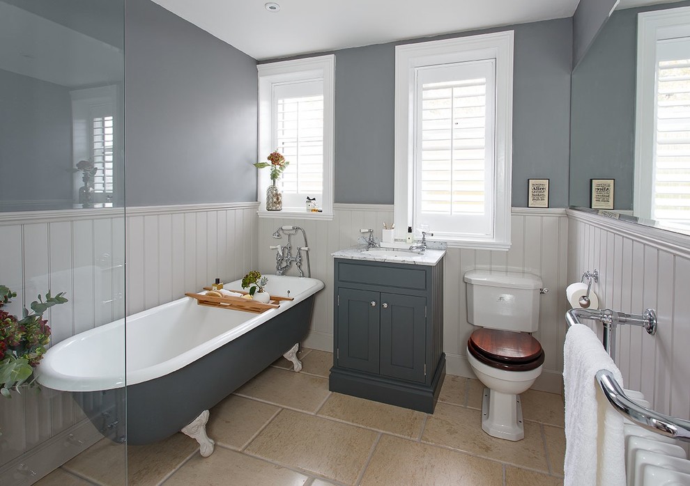 Design ideas for a mid-sized traditional bathroom in Edinburgh with shaker cabinets, grey cabinets, a freestanding tub, a two-piece toilet, beige tile, grey walls, an undermount sink, marble benchtops and limestone floors.