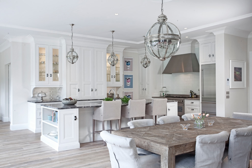 This is an example of a large traditional l-shaped open plan kitchen in Dublin with recessed-panel cabinets, white cabinets, marble benchtops, white splashback, glass tile splashback, stainless steel appliances, light hardwood floors and with island.