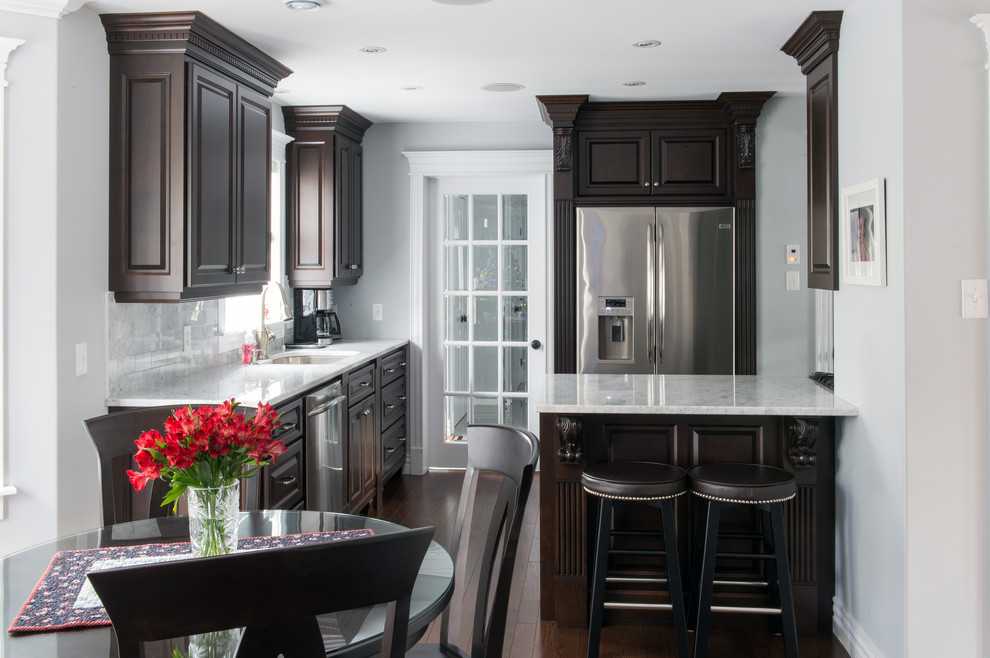 Example of a mid-sized transitional single-wall dark wood floor and brown floor enclosed kitchen design with an undermount sink, raised-panel cabinets, dark wood cabinets, marble countertops, gray backsplash, stone tile backsplash, stainless steel appliances and an island