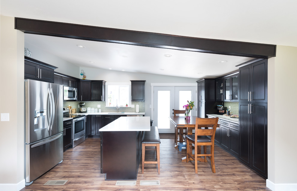 Photo of a mid-sized transitional l-shaped kitchen in Seattle with an undermount sink, beaded inset cabinets, dark wood cabinets, quartz benchtops, green splashback, ceramic splashback, stainless steel appliances, medium hardwood floors, with island and brown floor.
