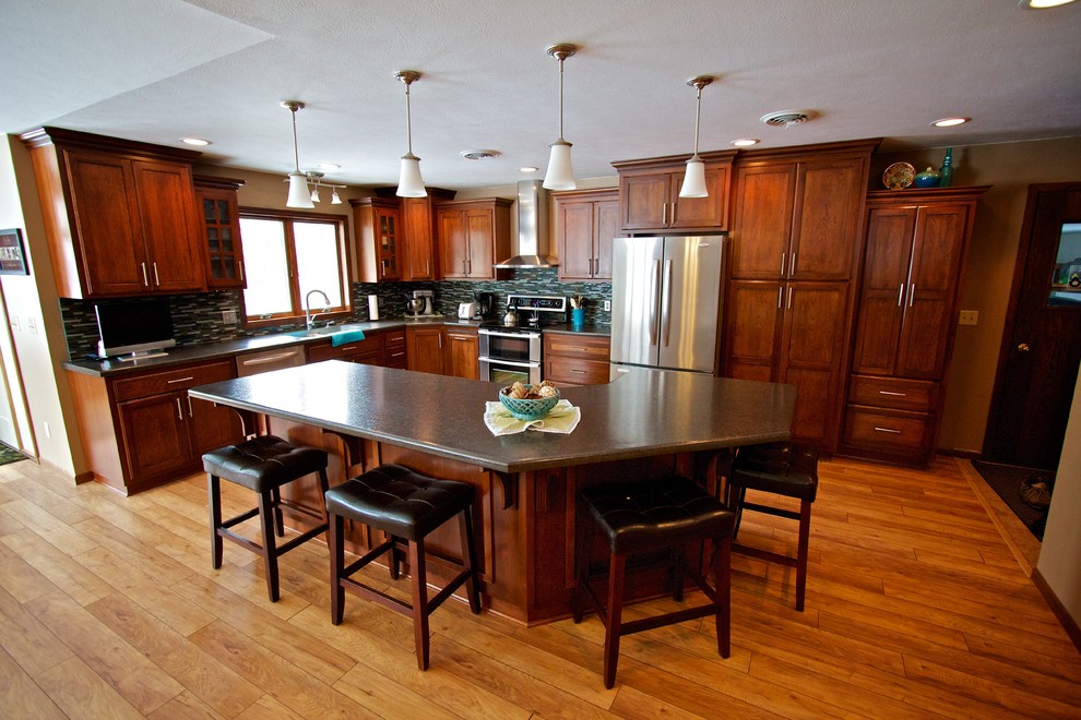 Example of a mid-sized l-shaped light wood floor open concept kitchen design with an undermount sink, shaker cabinets, dark wood cabinets, laminate countertops, multicolored backsplash, glass tile backsplash, stainless steel appliances and an island