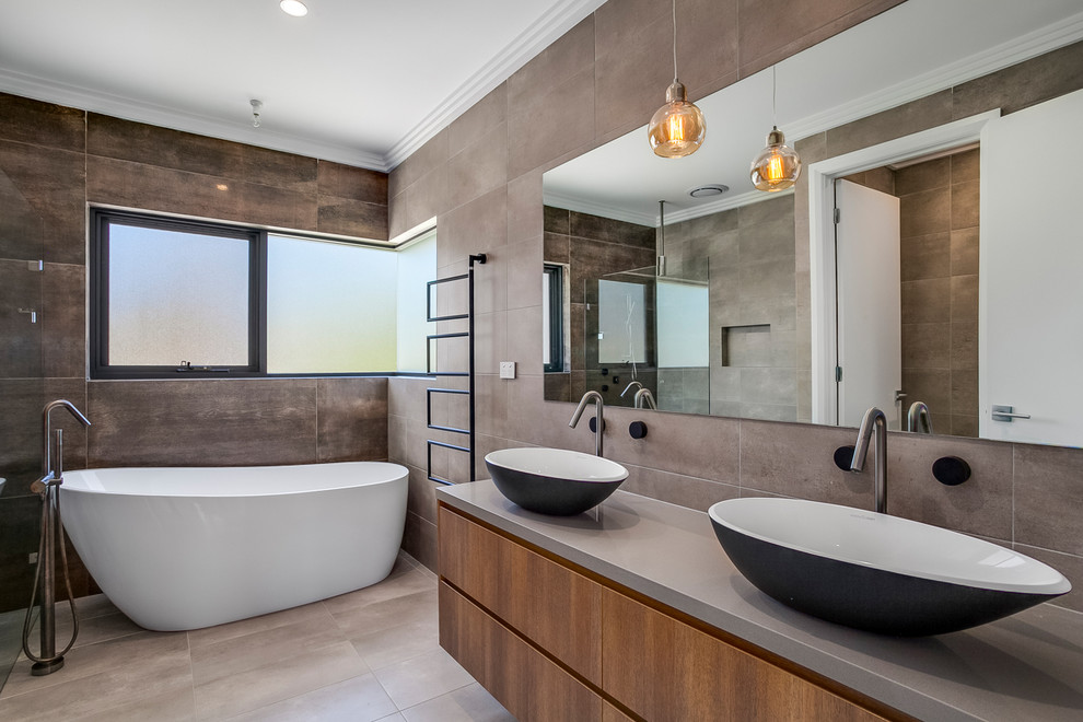 This is an example of a contemporary master bathroom in Sydney with flat-panel cabinets, brown cabinets, a freestanding tub, brown tile, gray tile, grey walls, a vessel sink, grey floor and grey benchtops.