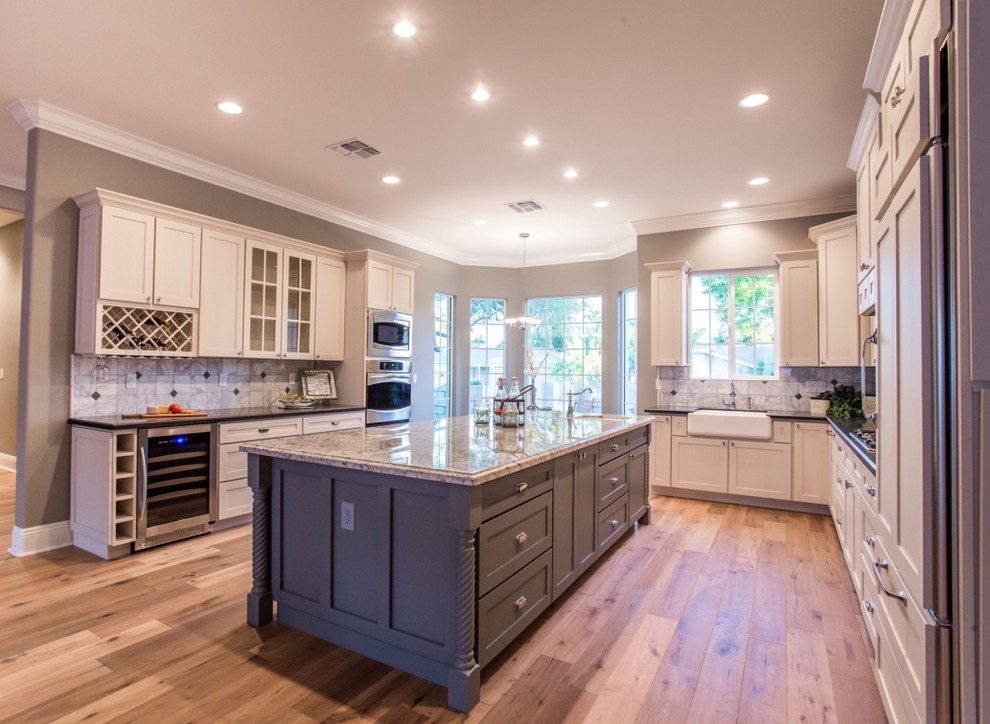 Photo of a large transitional l-shaped kitchen in Phoenix with a farmhouse sink, shaker cabinets, beige cabinets, granite benchtops, grey splashback, panelled appliances, medium hardwood floors, with island and brown floor.