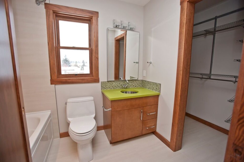 This is an example of a mid-sized eclectic 3/4 bathroom in Vancouver with flat-panel cabinets, dark wood cabinets, an alcove tub, a shower/bathtub combo, a one-piece toilet, grey walls, porcelain floors, an undermount sink, solid surface benchtops, grey floor and green benchtops.