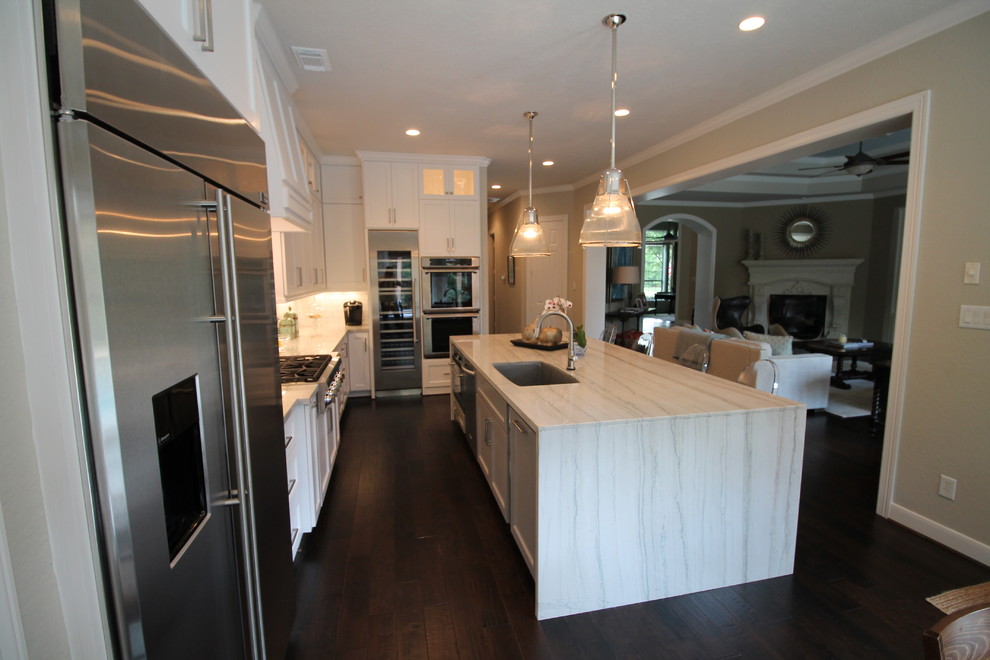 Inspiration for a large transitional l-shaped eat-in kitchen in Houston with white cabinets, white splashback, stainless steel appliances, dark hardwood floors, with island, a double-bowl sink, shaker cabinets, marble benchtops and subway tile splashback.