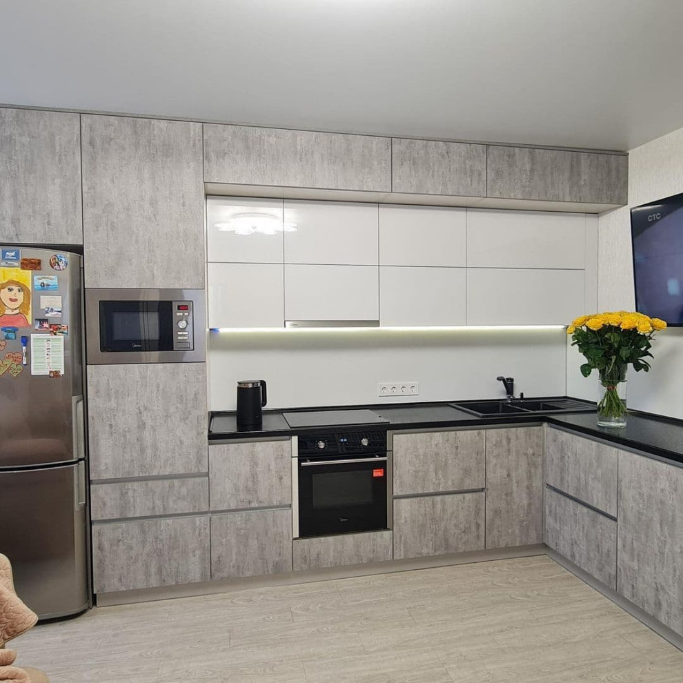 Photo of a large scandinavian l-shaped eat-in kitchen in Novosibirsk with a drop-in sink, flat-panel cabinets, grey cabinets, solid surface benchtops, white splashback, limestone splashback, black appliances, laminate floors, no island, yellow floor and black benchtop.