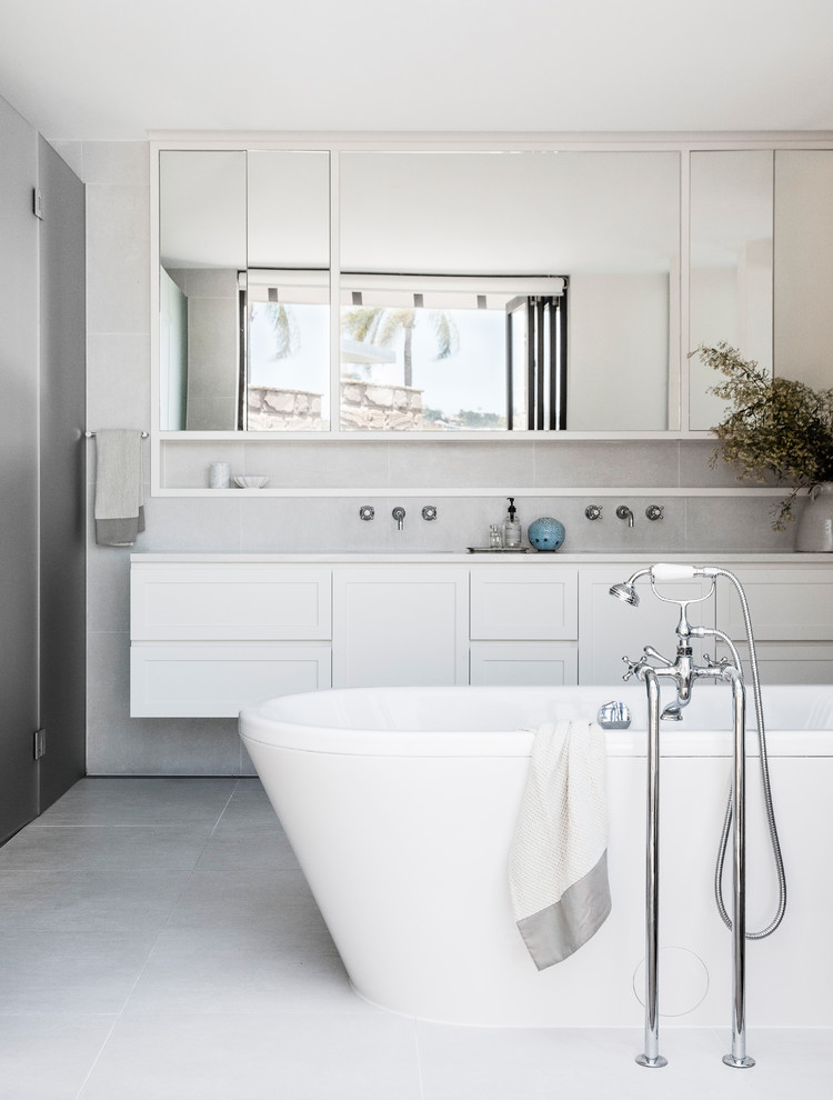 Design ideas for a transitional master bathroom in Sydney with shaker cabinets, white cabinets, a freestanding tub, an alcove shower, grey walls, a wall-mount sink, grey floor, a hinged shower door and white benchtops.