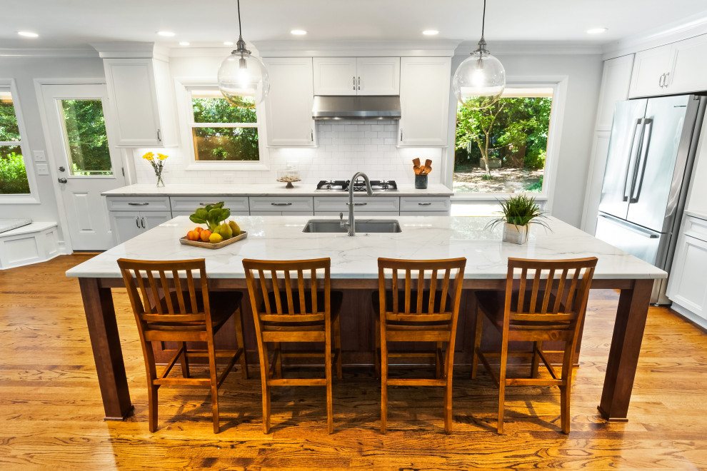 Example of a mid-sized transitional l-shaped medium tone wood floor and brown floor open concept kitchen design in Raleigh with a single-bowl sink, recessed-panel cabinets, white cabinets, quartzite countertops, white backsplash, porcelain backsplash, stainless steel appliances, an island and white countertops