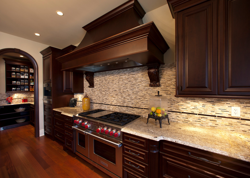 Huge mountain style u-shaped porcelain tile and beige floor open concept kitchen photo with an undermount sink, raised-panel cabinets, dark wood cabinets, granite countertops, red backsplash, porcelain backsplash, stainless steel appliances and a peninsula