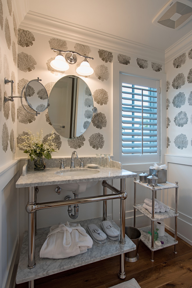 Foto på ett maritimt grå toalett, med öppna hyllor, grå skåp, flerfärgade väggar, mellanmörkt trägolv, ett undermonterad handfat, marmorbänkskiva och brunt golv