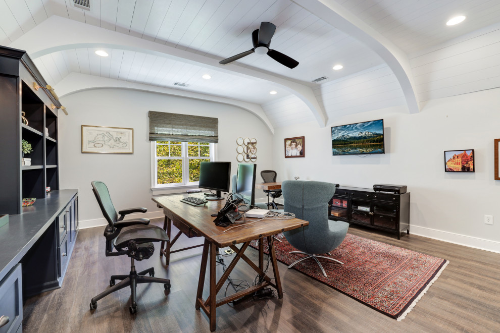 Klassisches Arbeitszimmer mit grauer Wandfarbe, braunem Holzboden, freistehendem Schreibtisch, braunem Boden, freigelegten Dachbalken, Holzdielendecke und gewölbter Decke in Sonstige