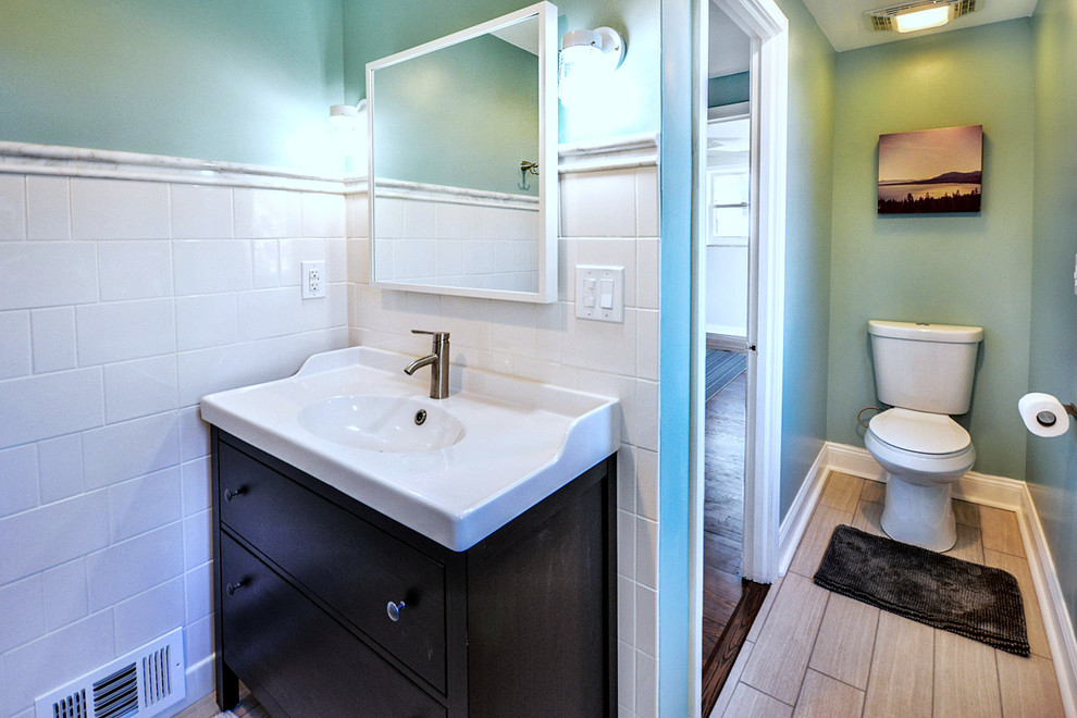 Photo of a small modern bathroom with flat-panel cabinets, dark wood cabinets, an alcove tub, a shower/bathtub combo, a two-piece toilet, white tile, ceramic tile, green walls, porcelain floors, an integrated sink, solid surface benchtops, grey floor, a shower curtain and white benchtops.