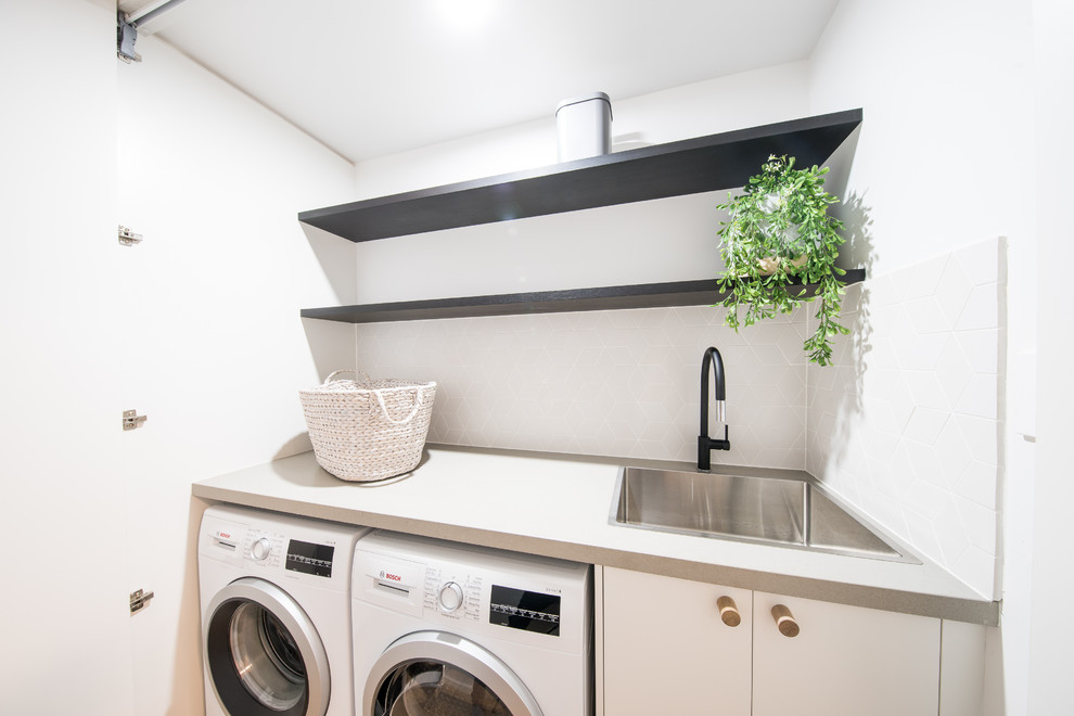 Inspiration for a mid-sized contemporary single-wall laundry cupboard in Central Coast with an integrated sink, flat-panel cabinets, white cabinets, quartz benchtops and a side-by-side washer and dryer.