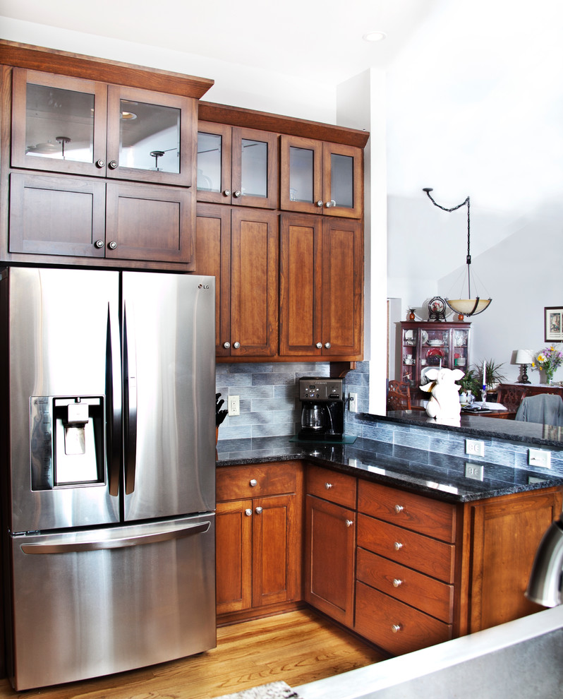Inspiration for a transitional l-shaped light wood floor open concept kitchen remodel in Milwaukee with a farmhouse sink, shaker cabinets, medium tone wood cabinets, granite countertops, gray backsplash, glass tile backsplash, stainless steel appliances and an island