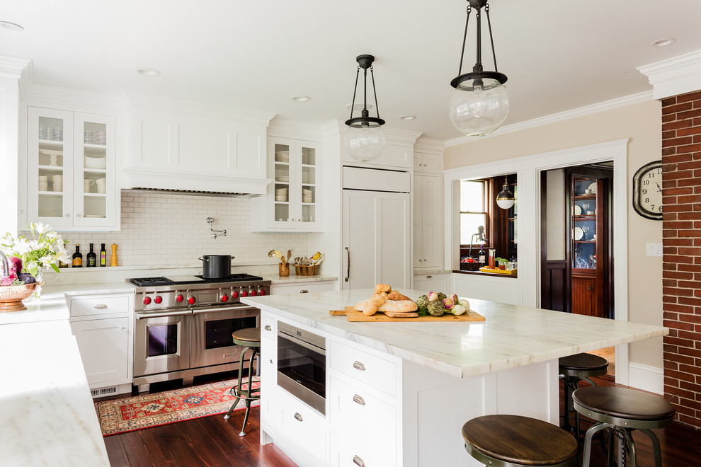 Example of a large classic l-shaped dark wood floor eat-in kitchen design in Boston with a farmhouse sink, raised-panel cabinets, white cabinets, marble countertops, white backsplash, subway tile backsplash, paneled appliances and an island