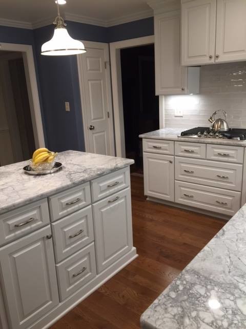 Photo of a mid-sized contemporary l-shaped eat-in kitchen in Raleigh with granite benchtops, an undermount sink, white cabinets, white splashback, subway tile splashback, stainless steel appliances, medium hardwood floors, with island and raised-panel cabinets.