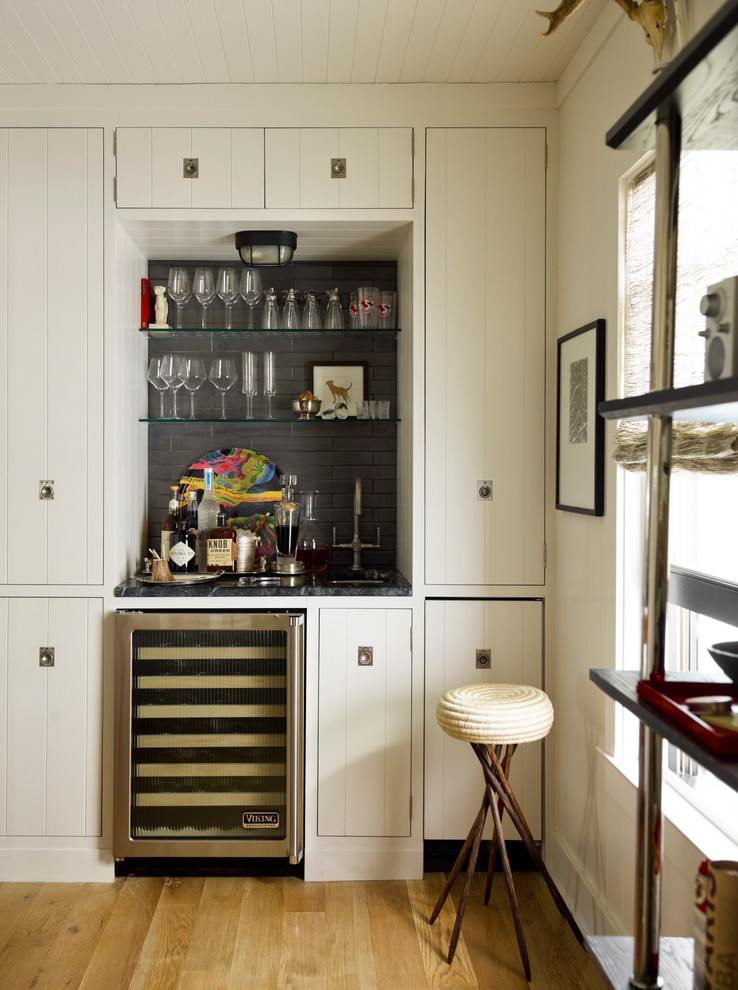 Inspiration for a small beach style single-wall wet bar in New York with medium hardwood floors, an undermount sink, flat-panel cabinets, white cabinets, grey splashback and beige floor.
