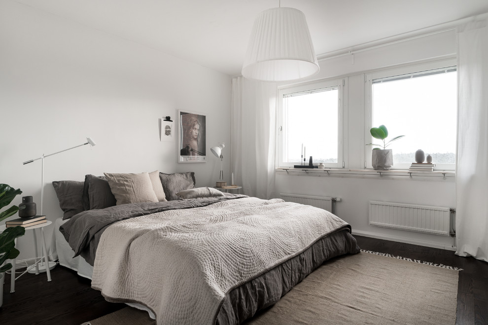 This is an example of a mid-sized scandinavian master bedroom in Stockholm with white walls, dark hardwood floors, no fireplace and brown floor.