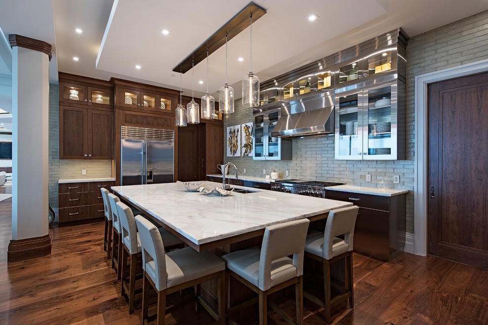 Photo of a contemporary l-shaped kitchen in Kansas City with an undermount sink, shaker cabinets, dark wood cabinets, grey splashback, glass tile splashback, stainless steel appliances, dark hardwood floors, with island, brown floor and white benchtop.