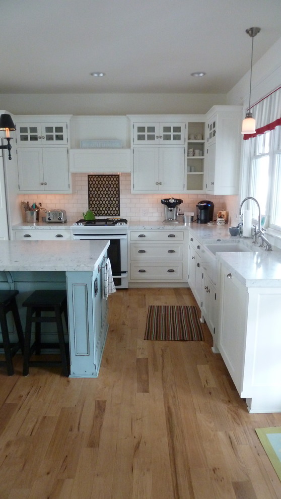 Design ideas for an expansive beach style l-shaped eat-in kitchen in Philadelphia with a farmhouse sink, recessed-panel cabinets, white cabinets, marble benchtops, white splashback, subway tile splashback, white appliances, medium hardwood floors and with island.