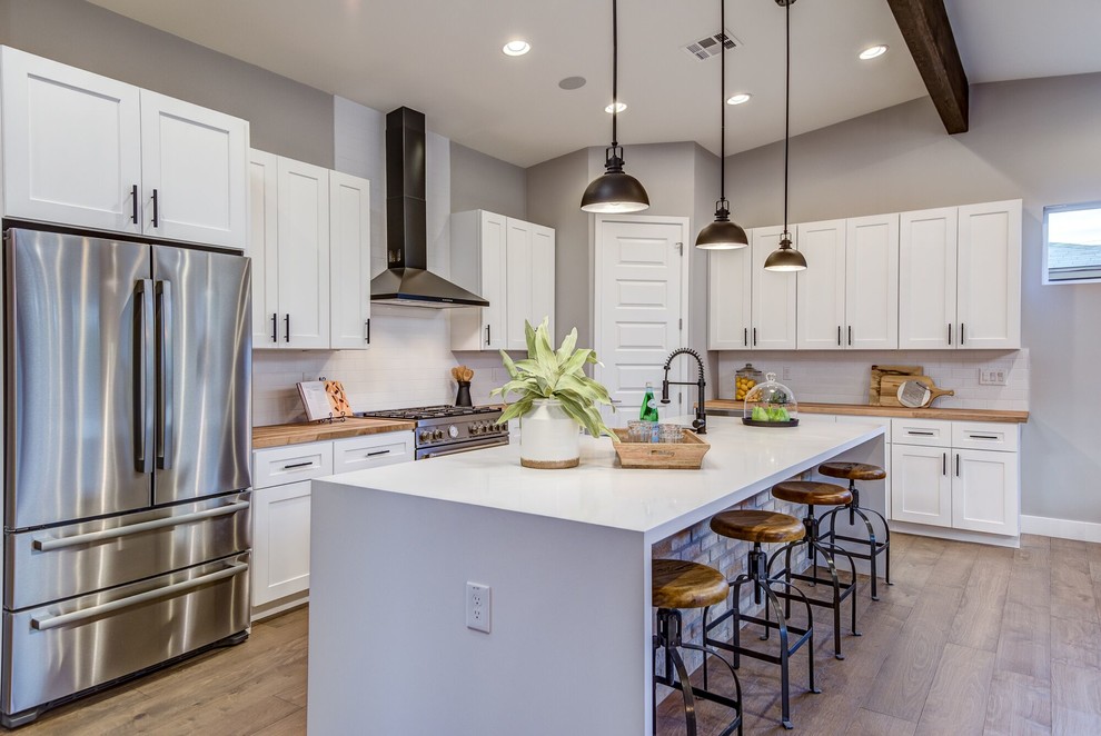 Transitional l-shaped kitchen in Phoenix with an undermount sink, shaker cabinets, white cabinets, wood benchtops, white splashback, stainless steel appliances, medium hardwood floors, with island, brown floor and brown benchtop.