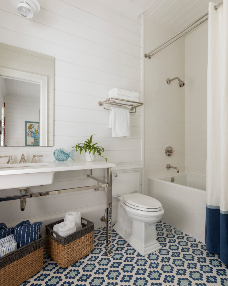This is an example of a mid-sized beach style 3/4 bathroom in Other with open cabinets, a shower/bathtub combo, a one-piece toilet, white walls, ceramic floors, a trough sink, marble benchtops, blue floor, a shower curtain, white benchtops, a single vanity, a freestanding vanity, timber and planked wall panelling.