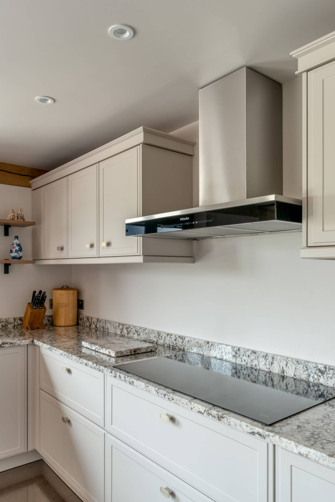 Foto på ett mellanstort funkis grå kök, med en undermonterad diskho, skåp i shakerstil, vita skåp, bänkskiva i kvartsit, vitt stänkskydd, svarta vitvaror, klinkergolv i keramik, en köksö och beiget golv
