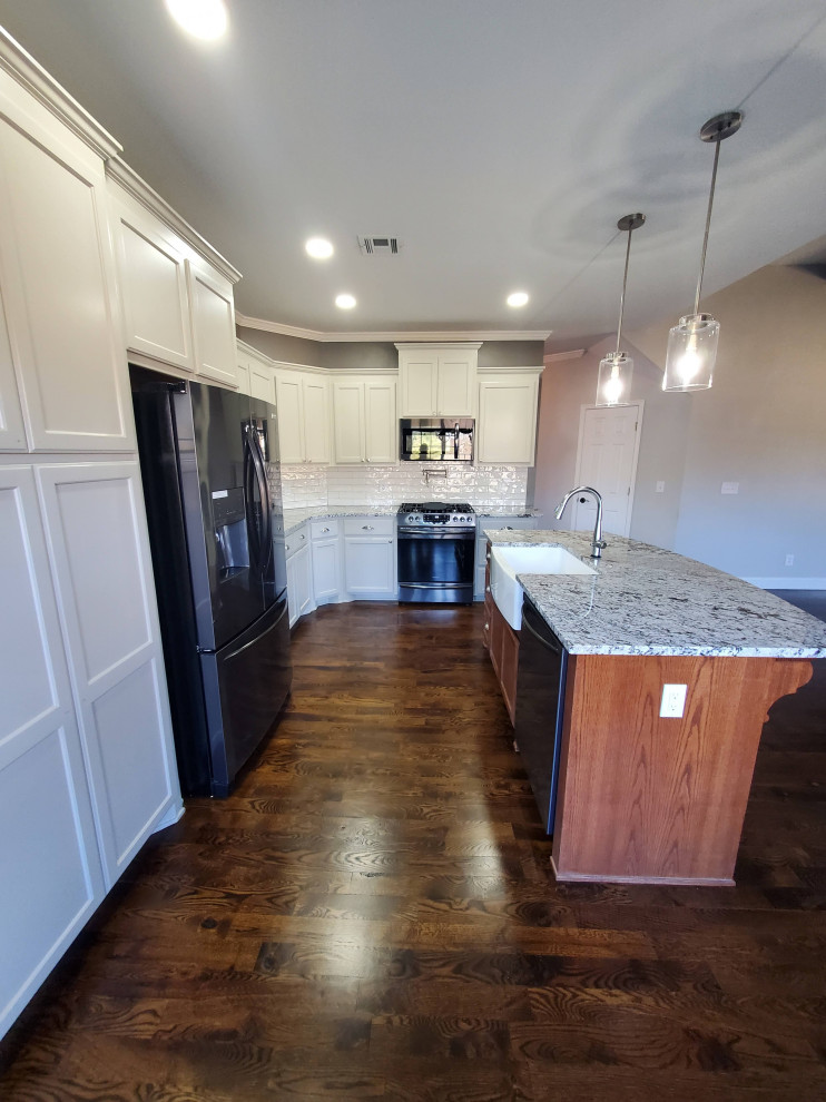 Example of a mid-sized trendy l-shaped dark wood floor, brown floor and wallpaper ceiling open concept kitchen design in Other with a farmhouse sink, beaded inset cabinets, white cabinets, granite countertops, white backsplash, glass tile backsplash, stainless steel appliances, an island and multicolored countertops