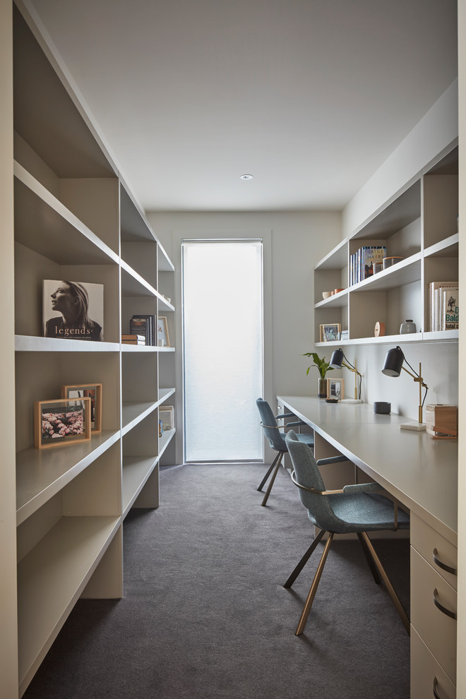 This is an example of a contemporary home office in Melbourne with white walls, carpet, a built-in desk and grey floor.