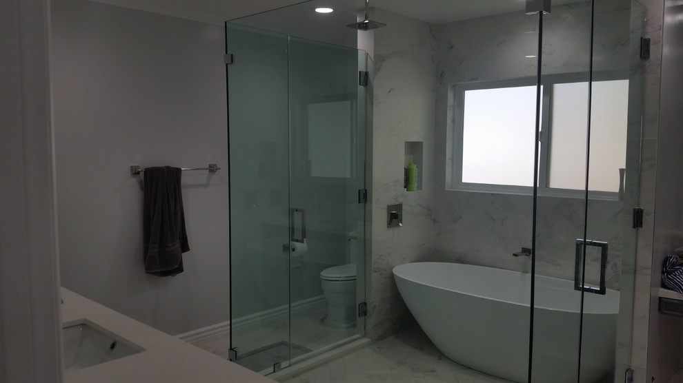 Photo of a mid-sized traditional kids bathroom in Los Angeles with raised-panel cabinets, grey cabinets, a freestanding tub, an alcove shower, a one-piece toilet, gray tile, marble, grey walls, marble floors, an undermount sink, concrete benchtops, grey floor, a hinged shower door and white benchtops.