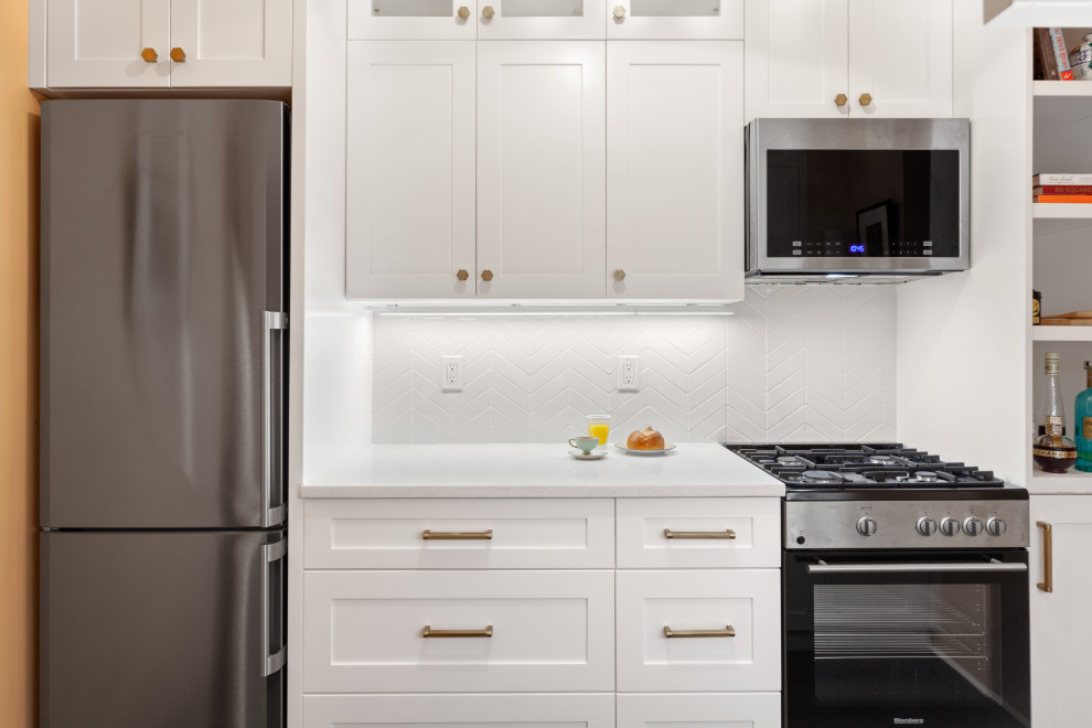 Example of a small trendy galley limestone floor and black floor enclosed kitchen design in New York with a single-bowl sink, shaker cabinets, white cabinets, solid surface countertops, white backsplash, porcelain backsplash, stainless steel appliances, no island and white countertops