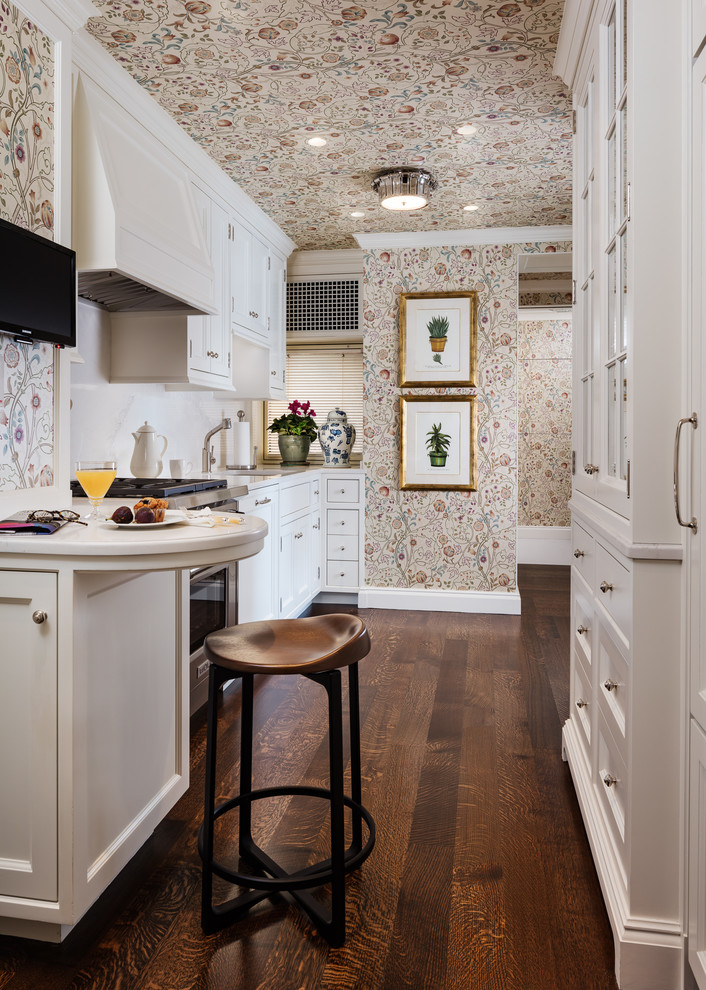 Photo of a traditional l-shaped kitchen in New York with an undermount sink, shaker cabinets, white cabinets, white splashback, dark hardwood floors, a peninsula and beige benchtop.