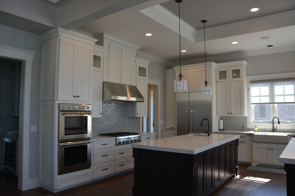 Inspiration for a large arts and crafts l-shaped eat-in kitchen in Chicago with a farmhouse sink, shaker cabinets, white cabinets, quartz benchtops, grey splashback, ceramic splashback, stainless steel appliances, medium hardwood floors and multiple islands.