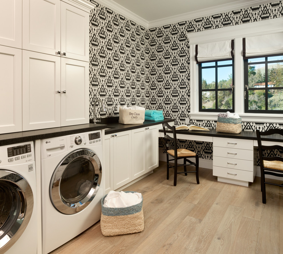 This is an example of a traditional l-shaped utility room in San Francisco with white cabinets, granite benchtops, light hardwood floors, a side-by-side washer and dryer, multi-coloured walls, black benchtop and recessed-panel cabinets.