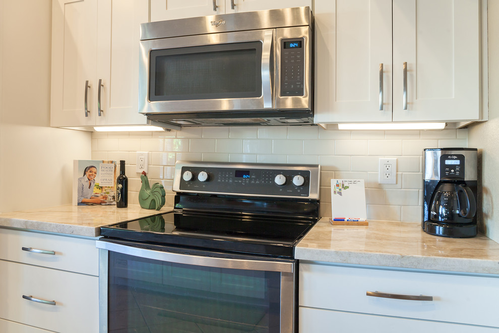Example of a transitional galley ceramic tile open concept kitchen design in Phoenix with an undermount sink, recessed-panel cabinets, white cabinets, quartz countertops, white backsplash, ceramic backsplash, stainless steel appliances and an island