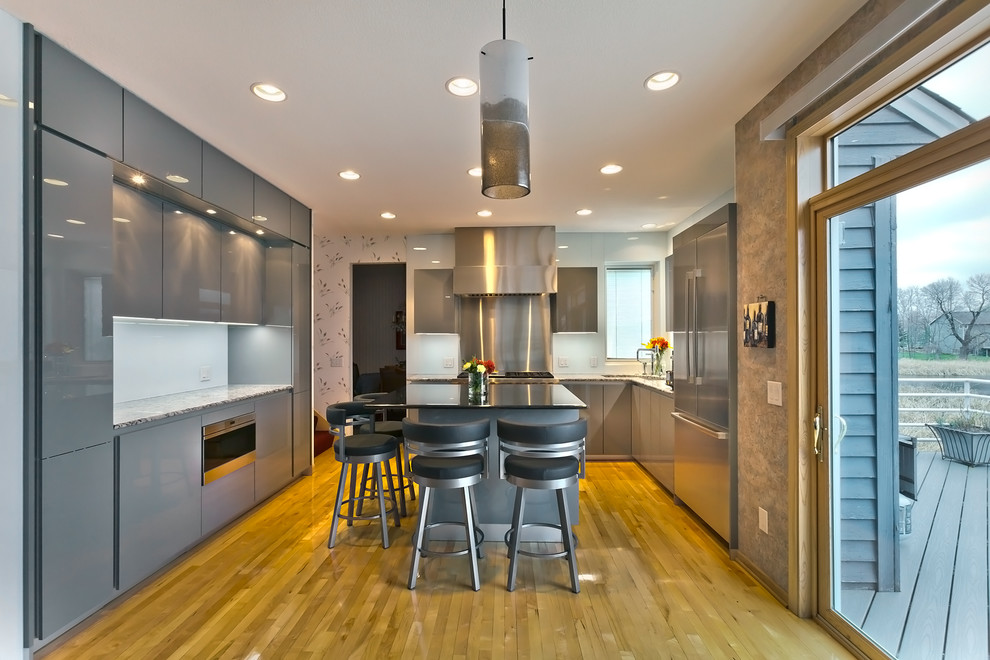 Mid-sized contemporary l-shaped eat-in kitchen in Minneapolis with an undermount sink, flat-panel cabinets, grey cabinets, granite benchtops, white splashback, glass sheet splashback, stainless steel appliances, light hardwood floors and with island.