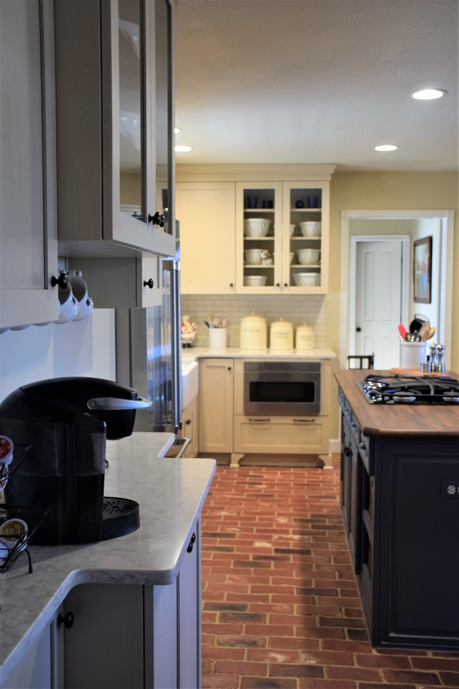 Example of a mid-sized transitional u-shaped brick floor eat-in kitchen design with a farmhouse sink, shaker cabinets, white cabinets, quartzite countertops, white backsplash, subway tile backsplash, stainless steel appliances and an island